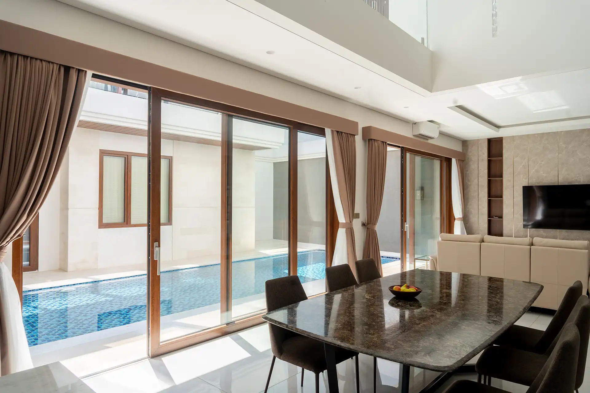 View from the living room to the pool at a private residence in Cipete, South Jakarta, featuring realistic walnut wood decor soundproof UPVC Lift&Slide sliding doors with Low-E insulated double glazing.